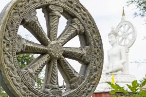 Wheel of dharma with Buddha statue in background